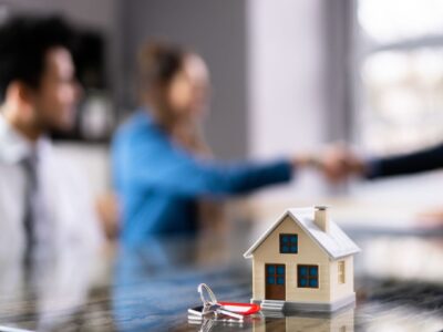 Home buyers shaking hands with mortgage advisor with toy house and keys in foreground