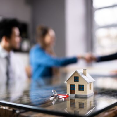 Home buyers shaking hands with mortgage advisor with toy house and keys in foreground